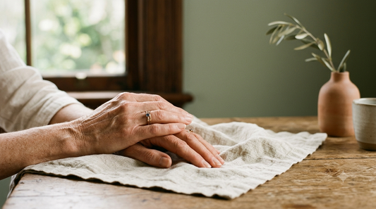 Mature hands with crepey, thinning skin resting on a linen cloth by a window